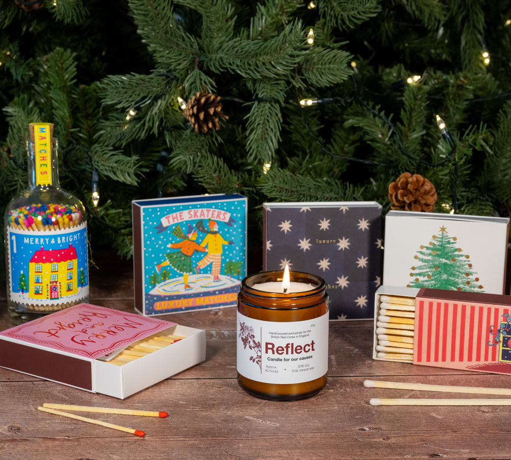 Image of different presents in front of a christmas tree including a reflect candle and boxes of matches