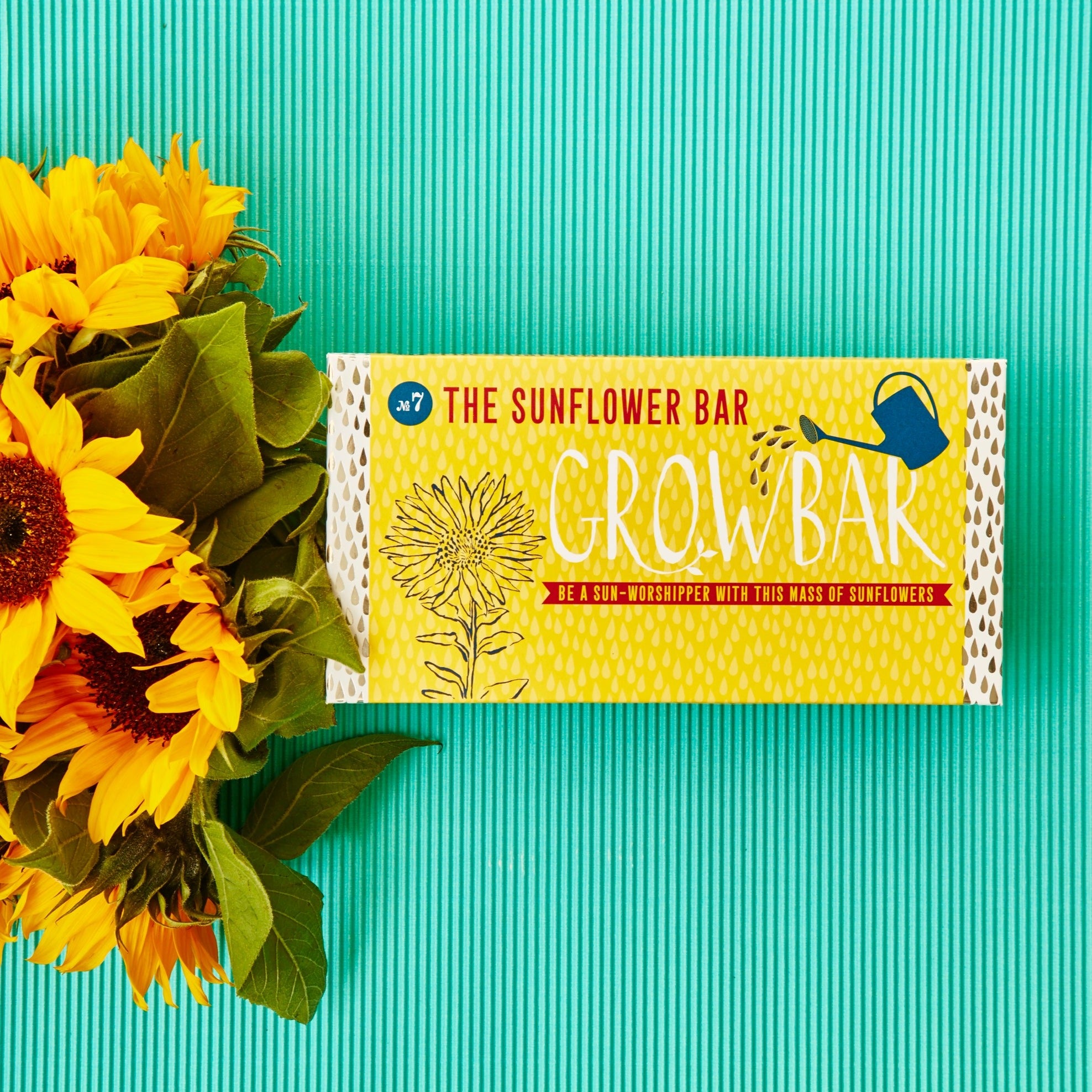 Packaging of 'The Sunflower Bar' growbar with a vibrant sunflower behind it, set against a striped teal background.
