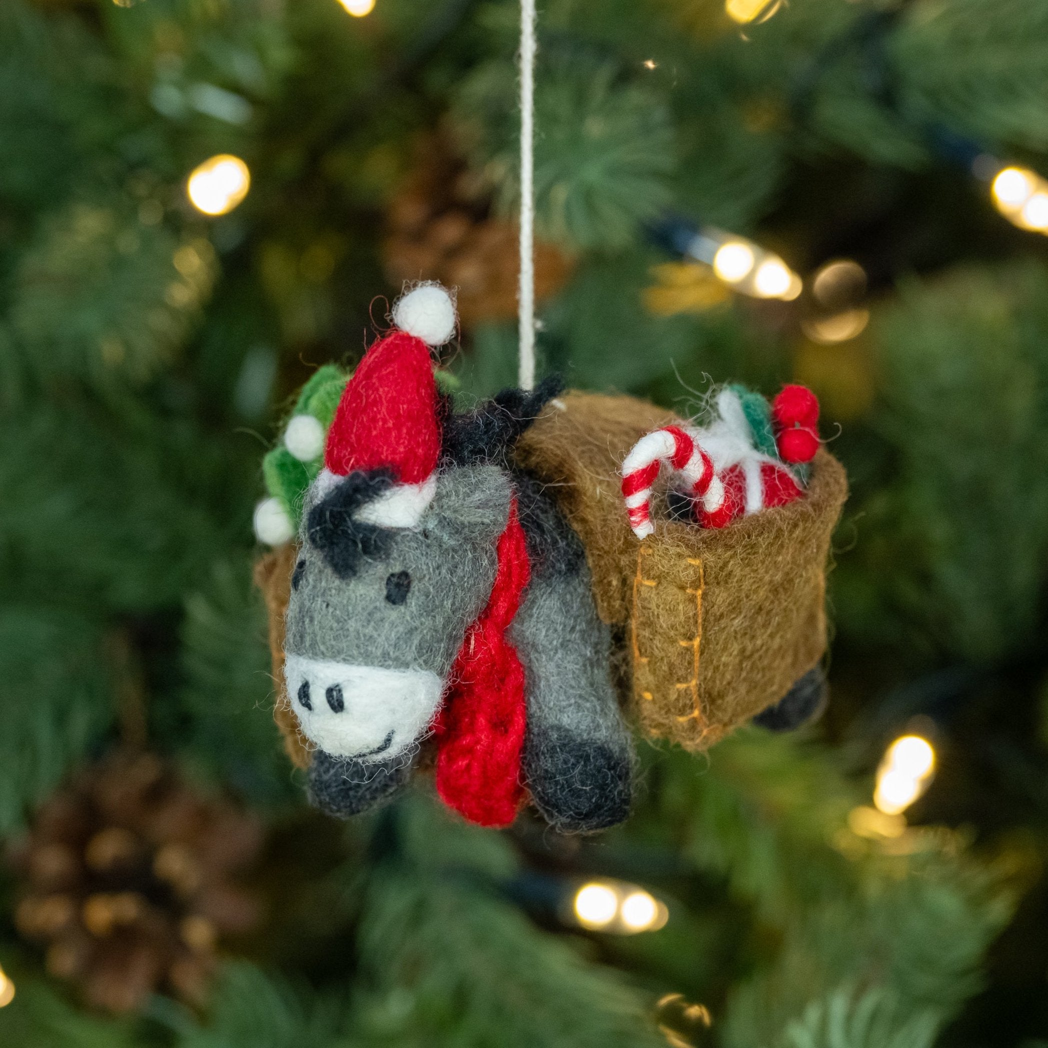 Handmade felt donkey Christmas decoration with Christmas panniers loaded with festive items, hanging on a Christmas tree.