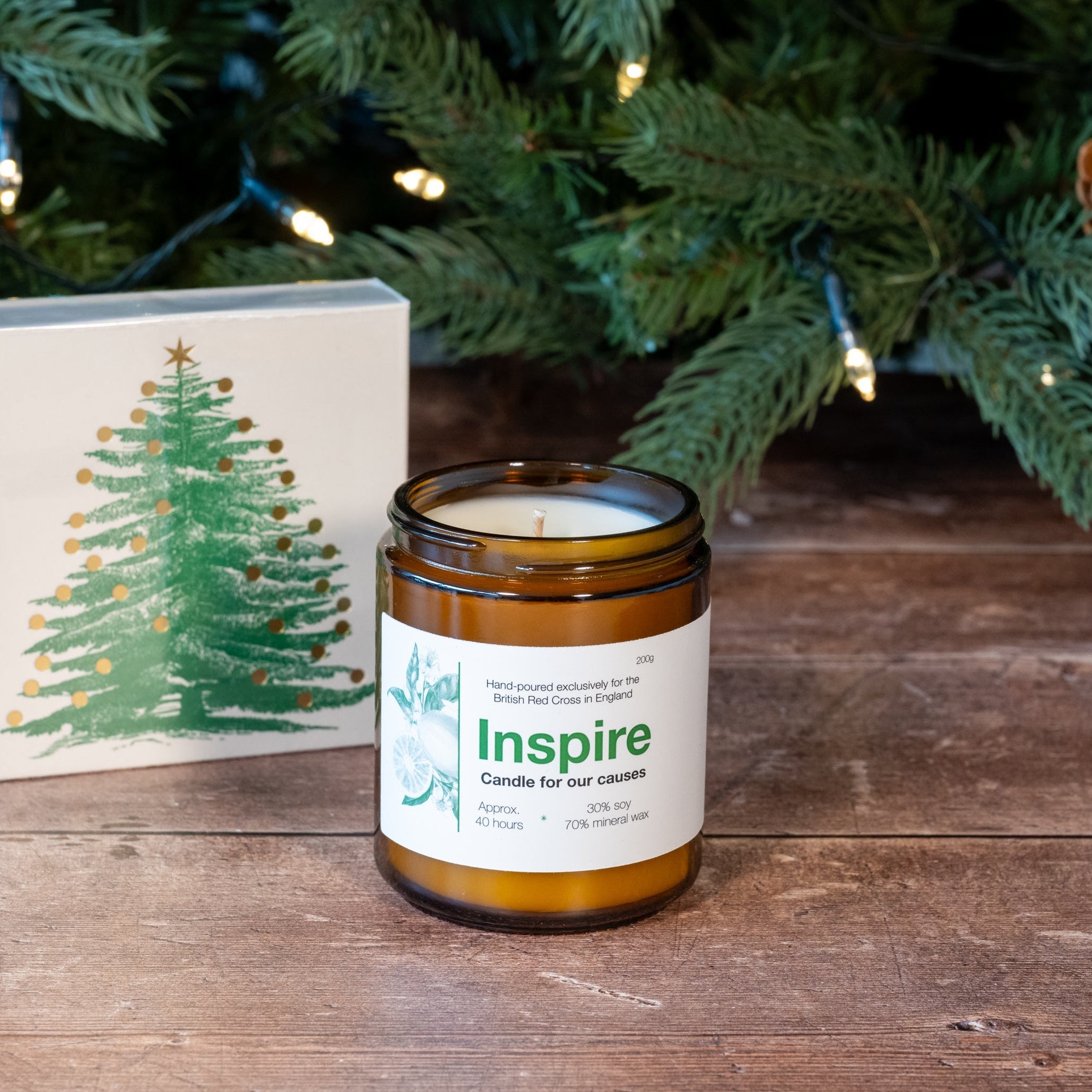 Candle labeled 'Inspire' on a wooden surface with a Christmas tree in the background