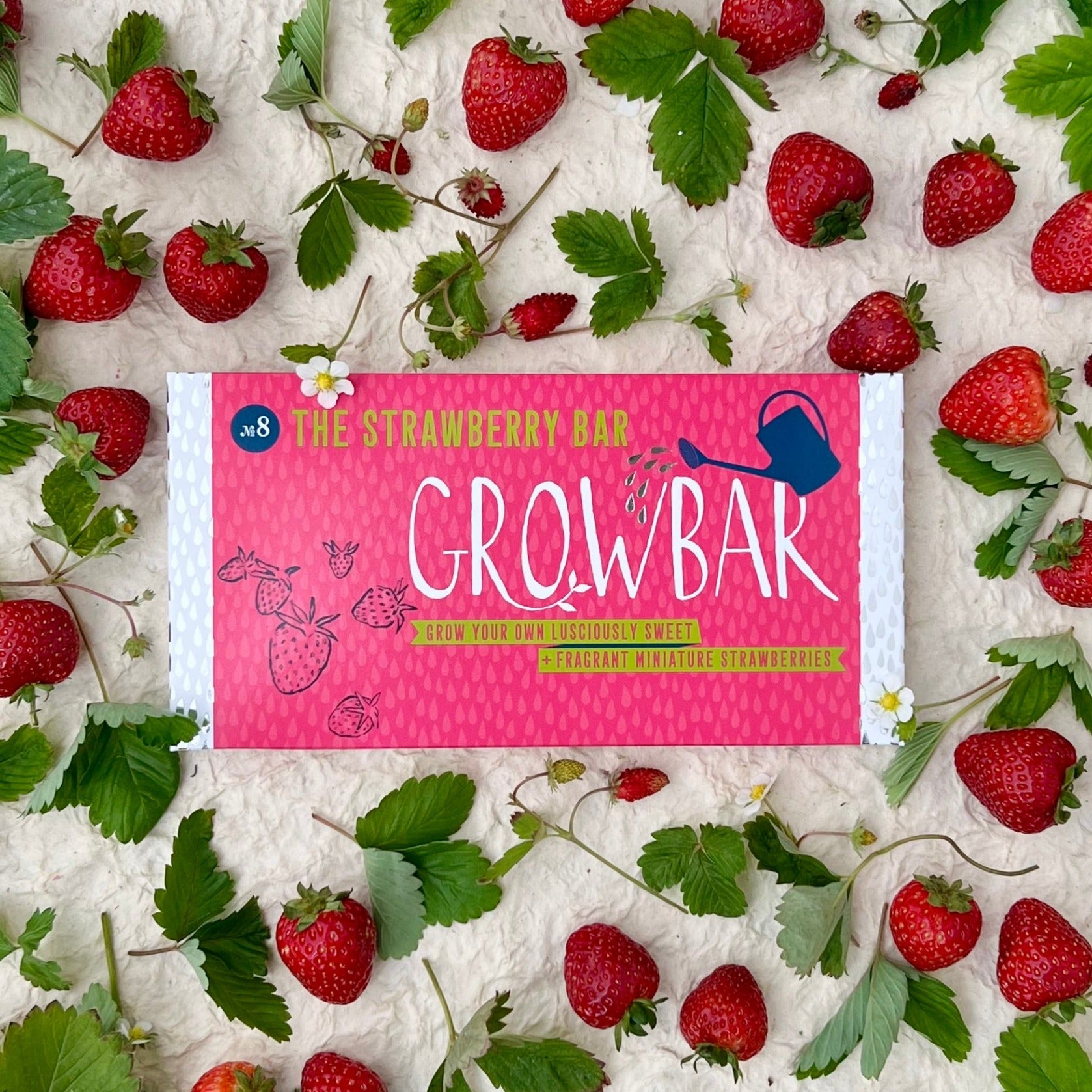 The image shows a box of 'Growbar - The Strawberry Bar' surrounded by fresh strawberries and green leaves on a white surface.