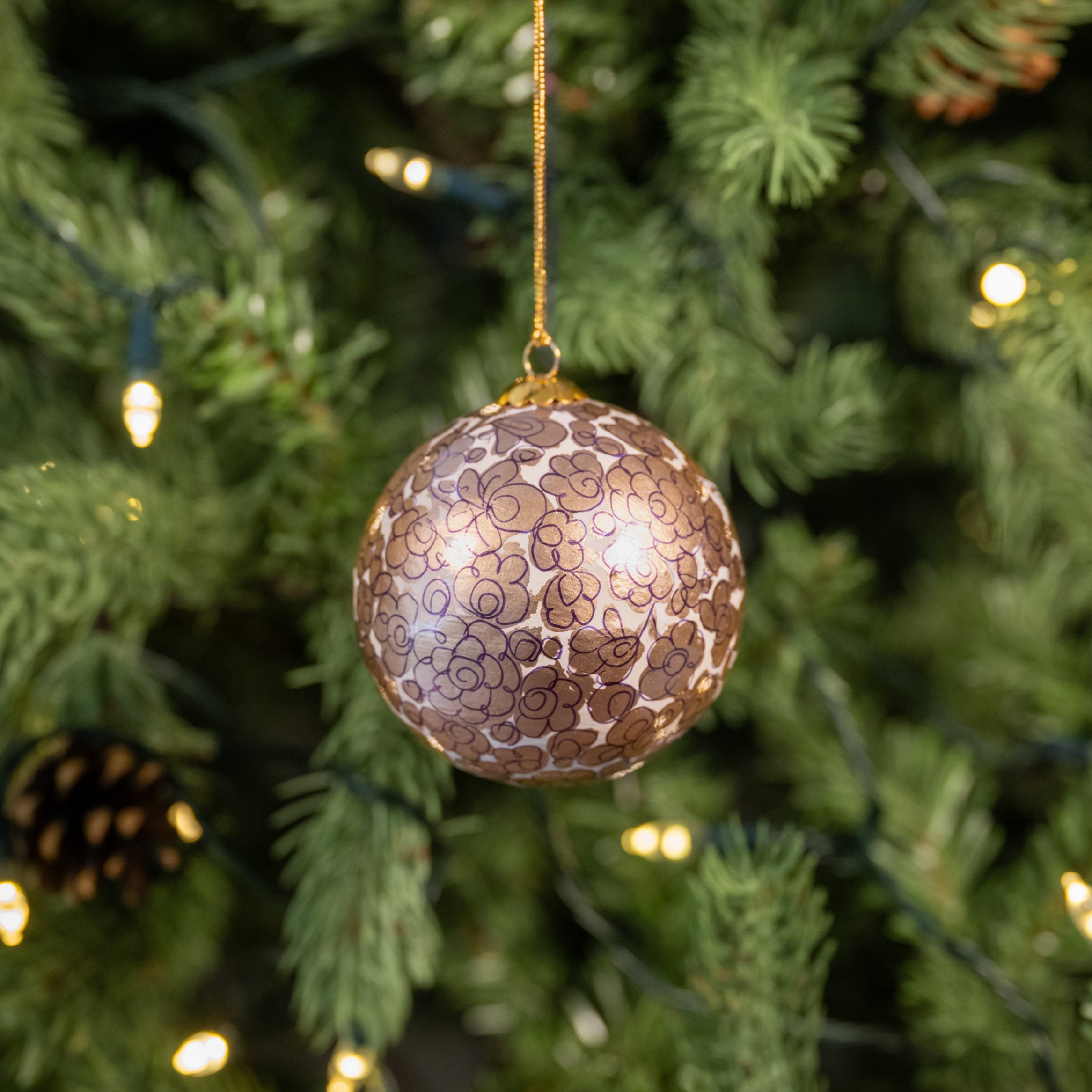 Decorative ornament on a Christmas tree with lights and pine cones.