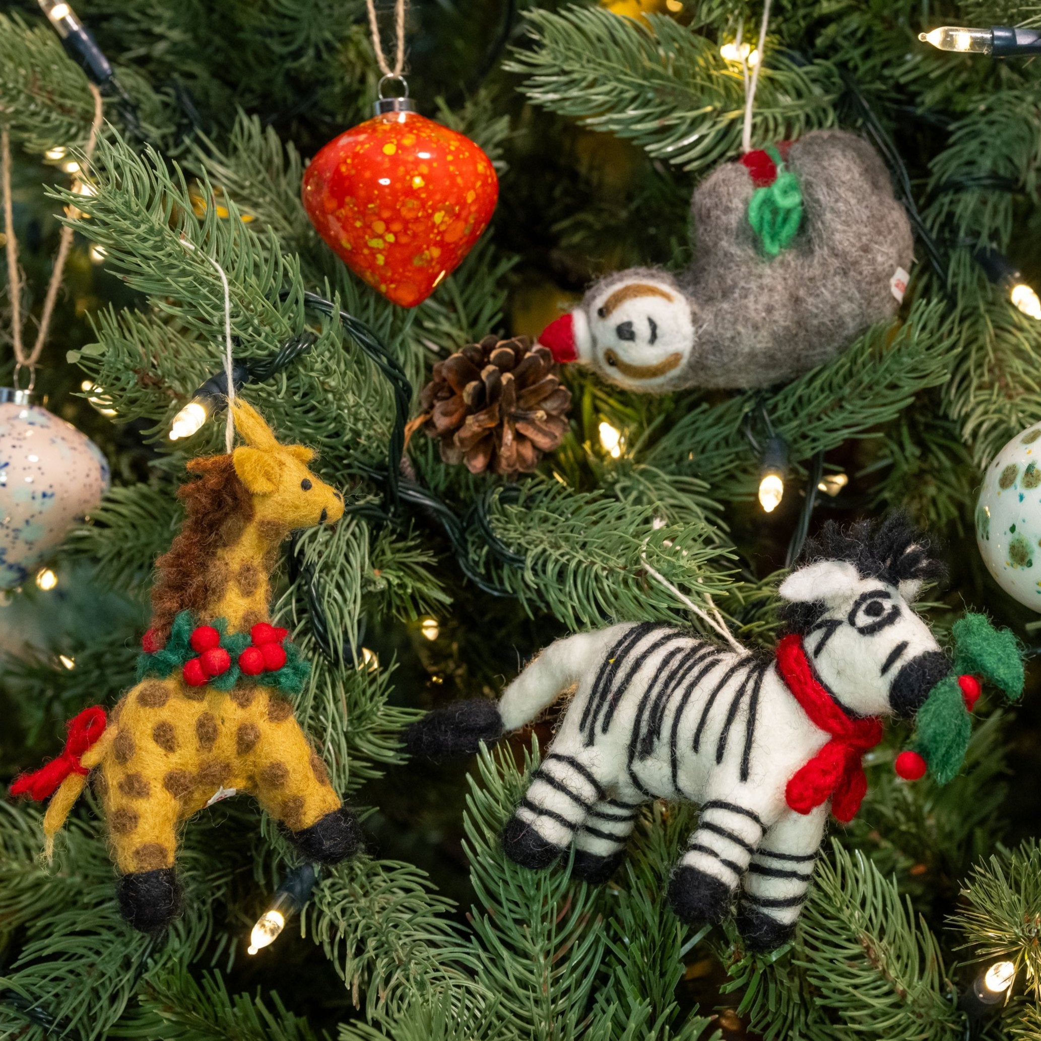 View of Giraffe with Holly Wreath Decoration, Zebra with sprig, Sloth in hat & baubles on a Christmas tree