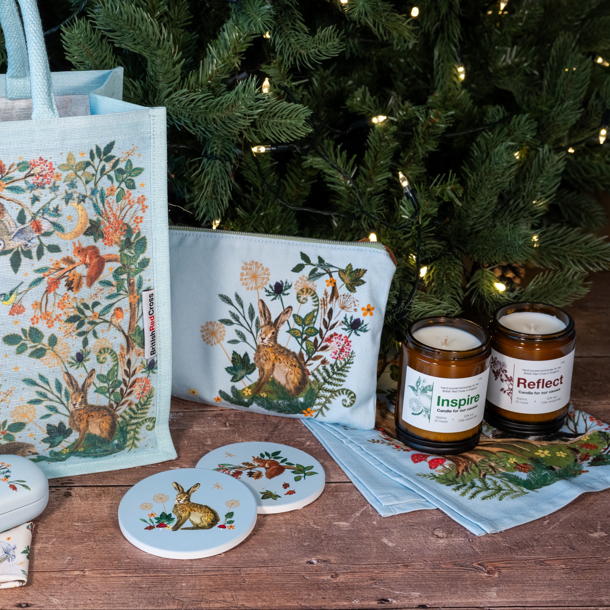 Decorative items including a bag, coasters, and candles with nature-themed designs in front of a Christmas tree.