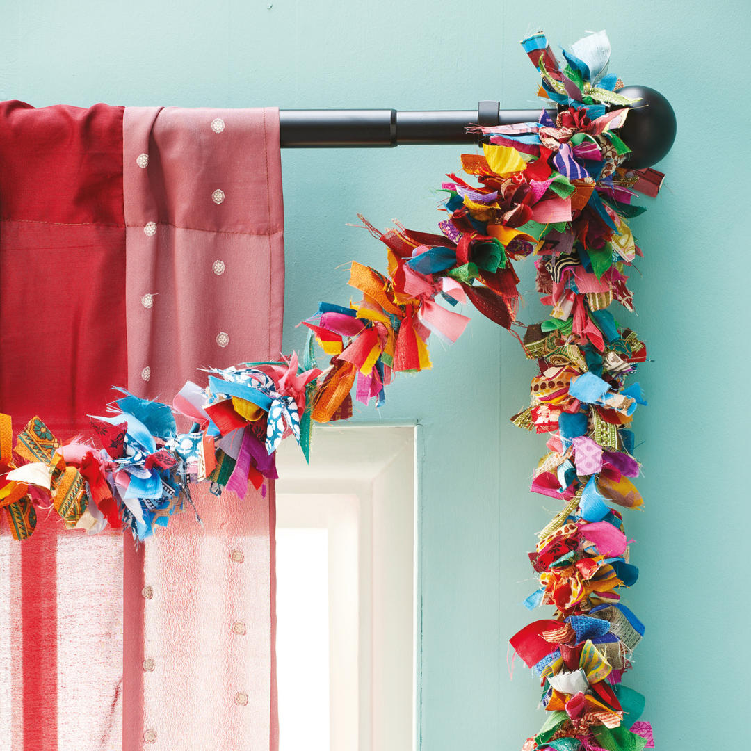 Colorful fabric garland hanging on a curtain rod with a light blue wall background.